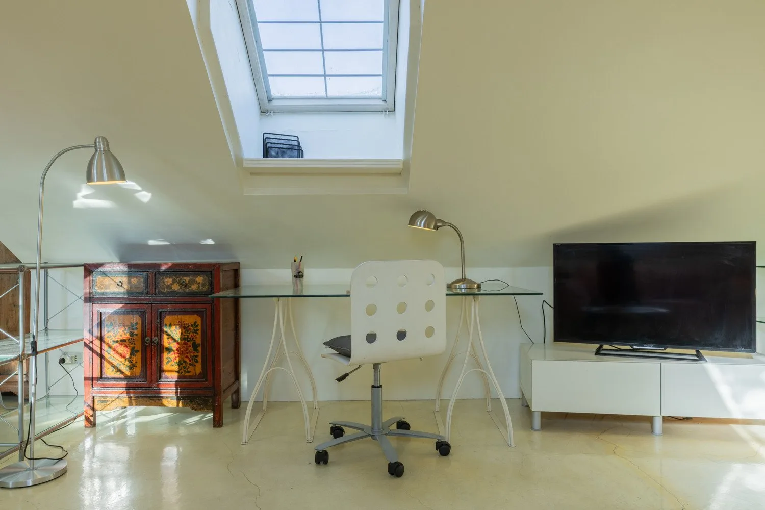 Un espacio de trabajo abuhardillado y luminoso con escritorio, silla, televisor y tragaluz.