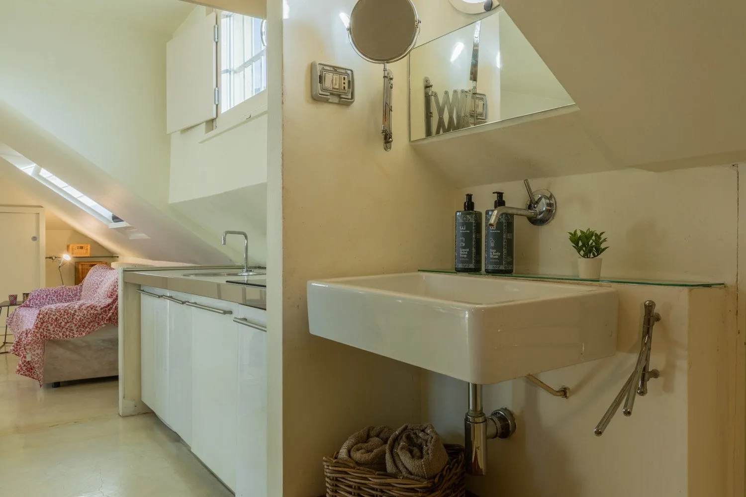 Un baño con lavabo suspendido y espejo junto a una zona de descanso con techo inclinado.