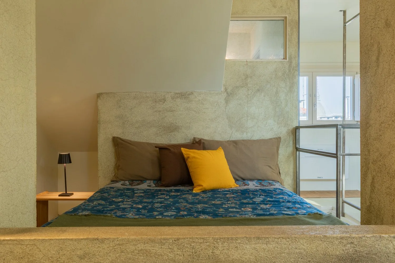 A bedroom with a bed dressed in blue patterned bedding and a yellow pillow.