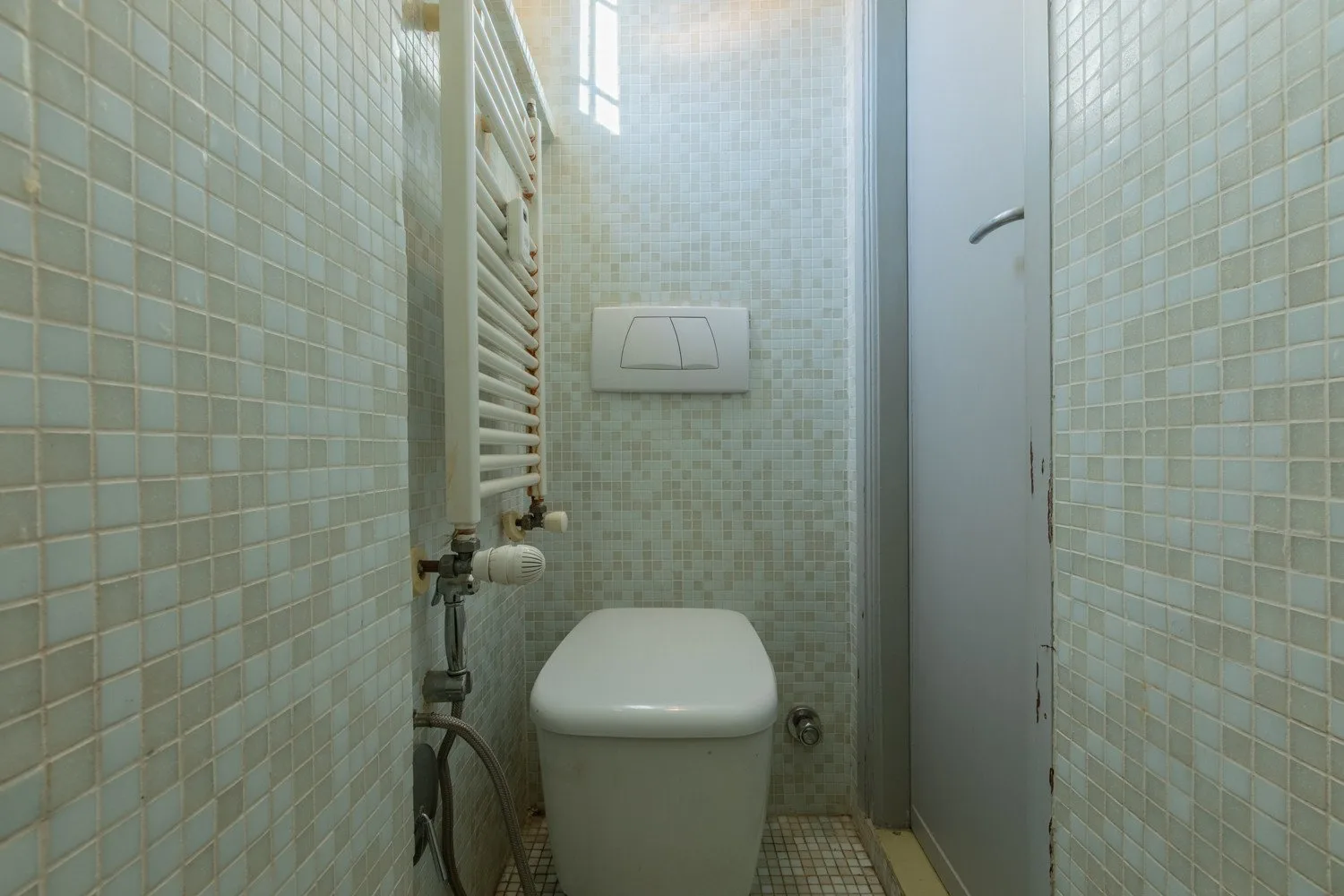 Un baño con azulejos, un inodoro, un panel de descarga y una puerta estrecha.