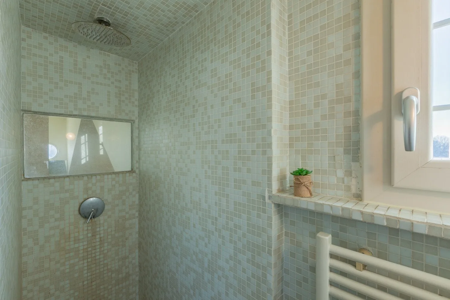 Un baño revestido de azulejos con una ducha de pared y una ventana.