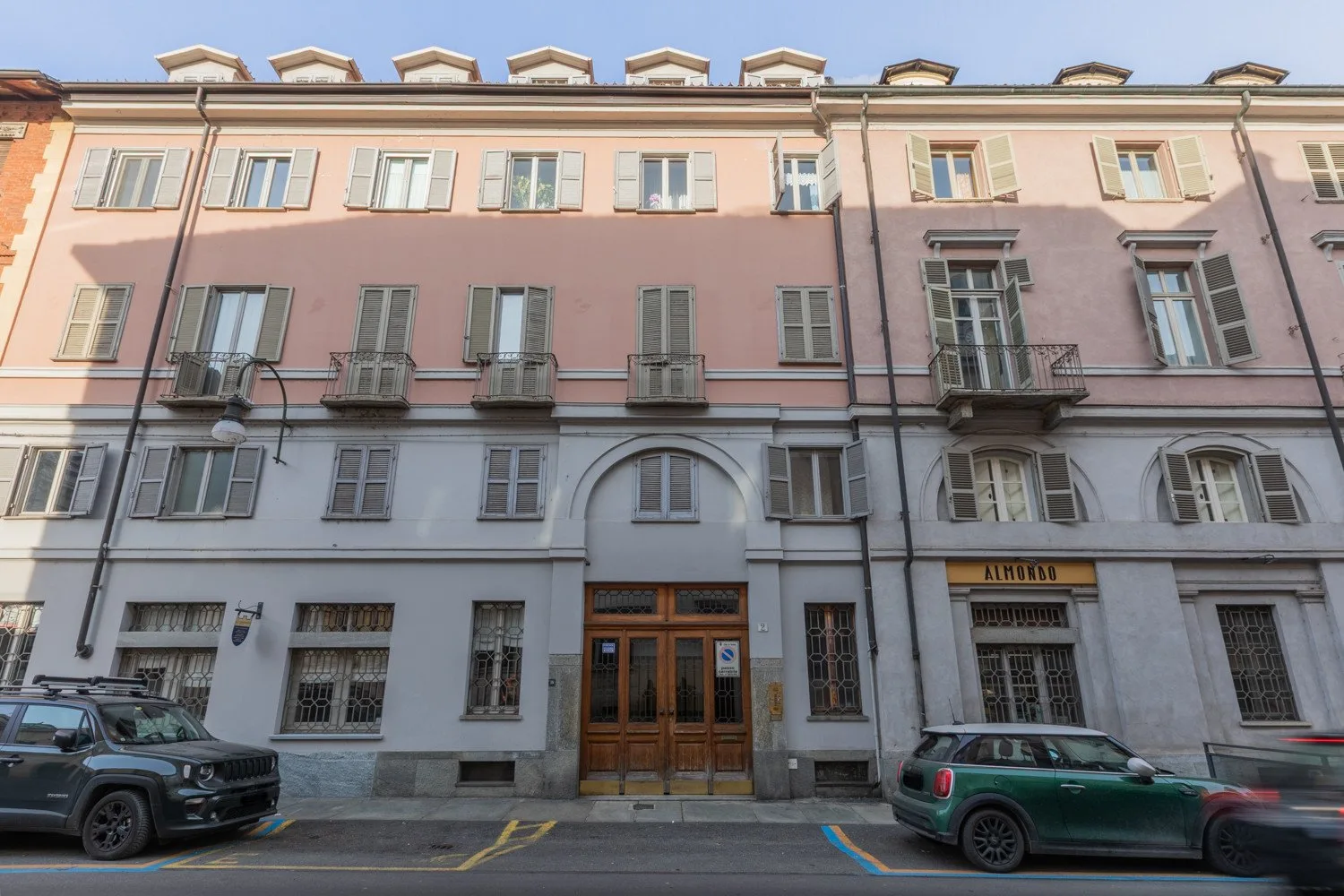 Fachada de un edificio de varias plantas con ventanas con contraventanas, balcones y entradas a nivel de calle.