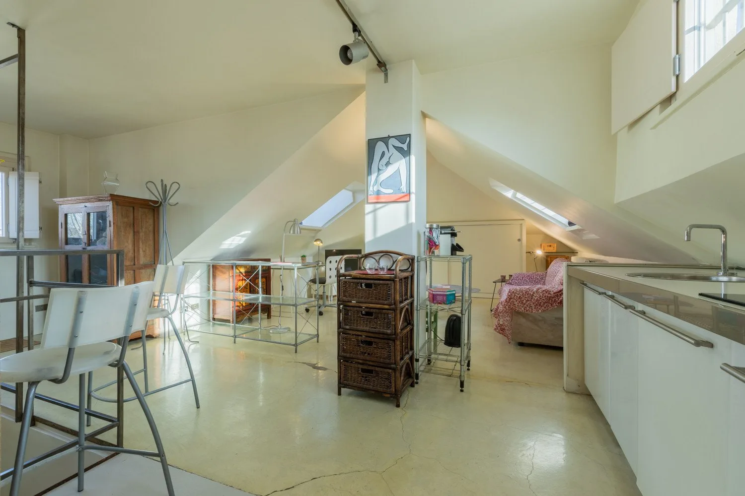 A bright attic room with a bed, a dining table, and kitchenette cabinets.