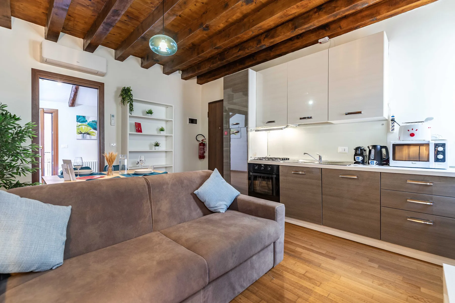 Una sala de estar se abre a una cocina compacta, con un sofá bajo vigas de madera vistas.