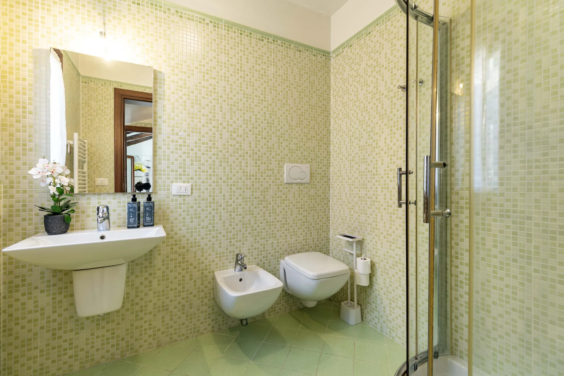 Un baño con azulejos, lavabo, inodoro, bidé y ducha de vidrio.