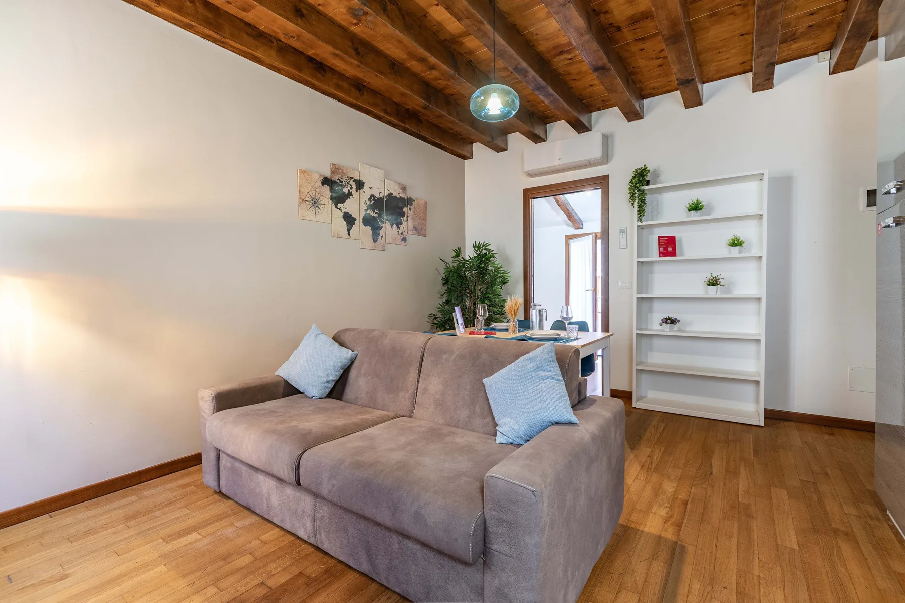 Una sala de estar con sofá seccional, estantería blanca y vigas de madera expuestas.