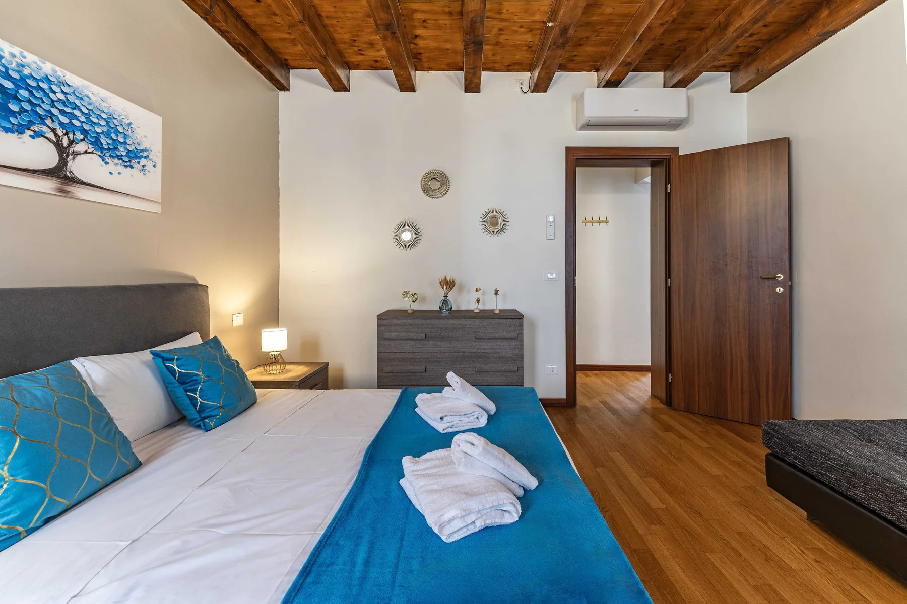 Un dormitorio con una cama, vigas de madera en el techo y una puerta abierta.