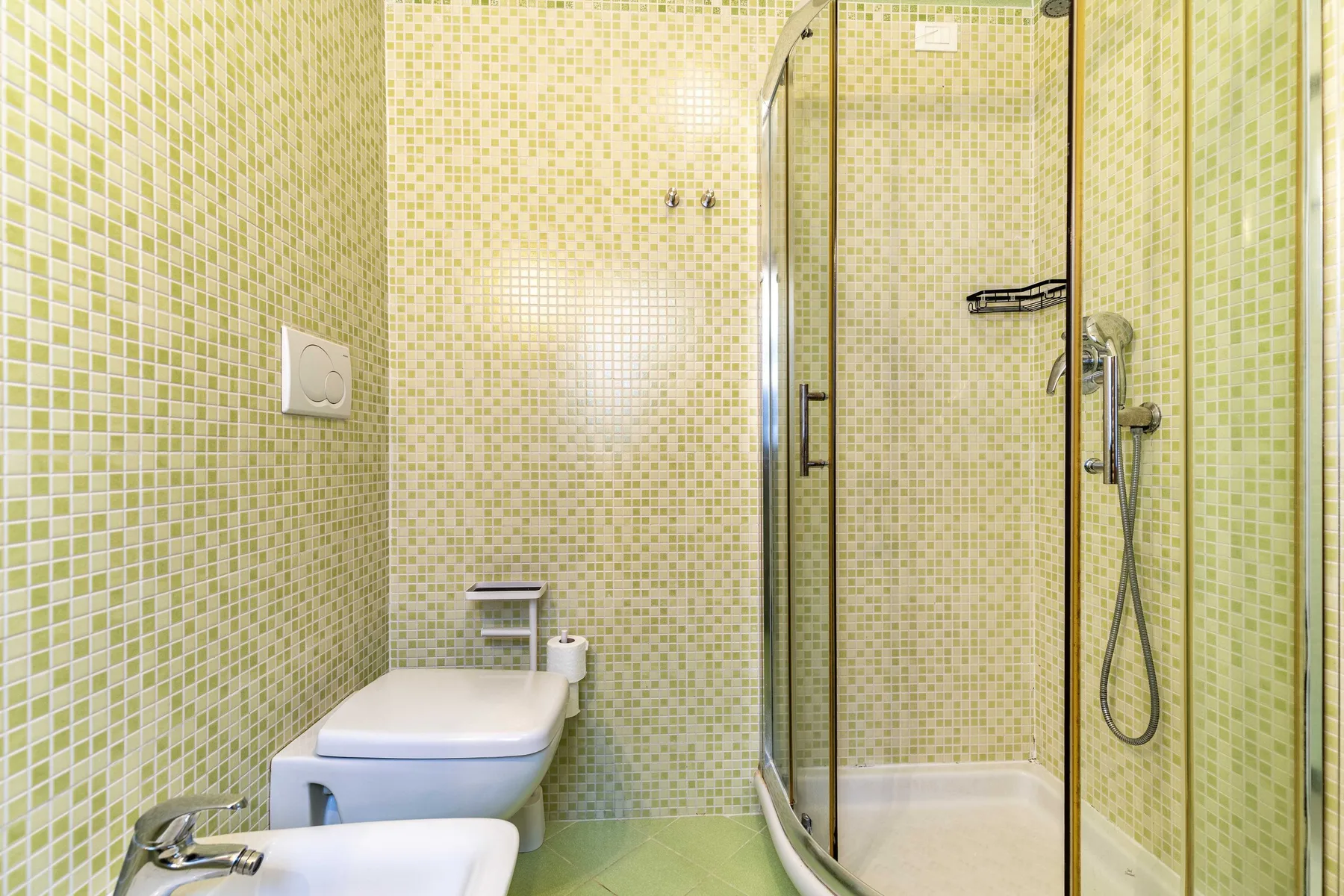 Un baño alicatado con una ducha de vidrio y accesorios blancos.