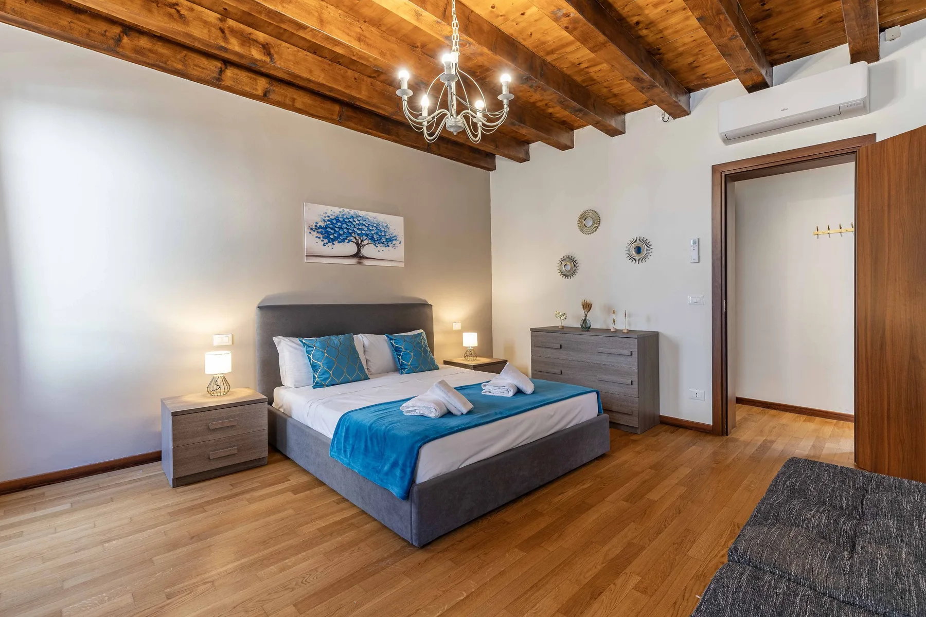 Un dormitorio con una cama vestida con ropa de cama azul y vigas de madera en el techo.