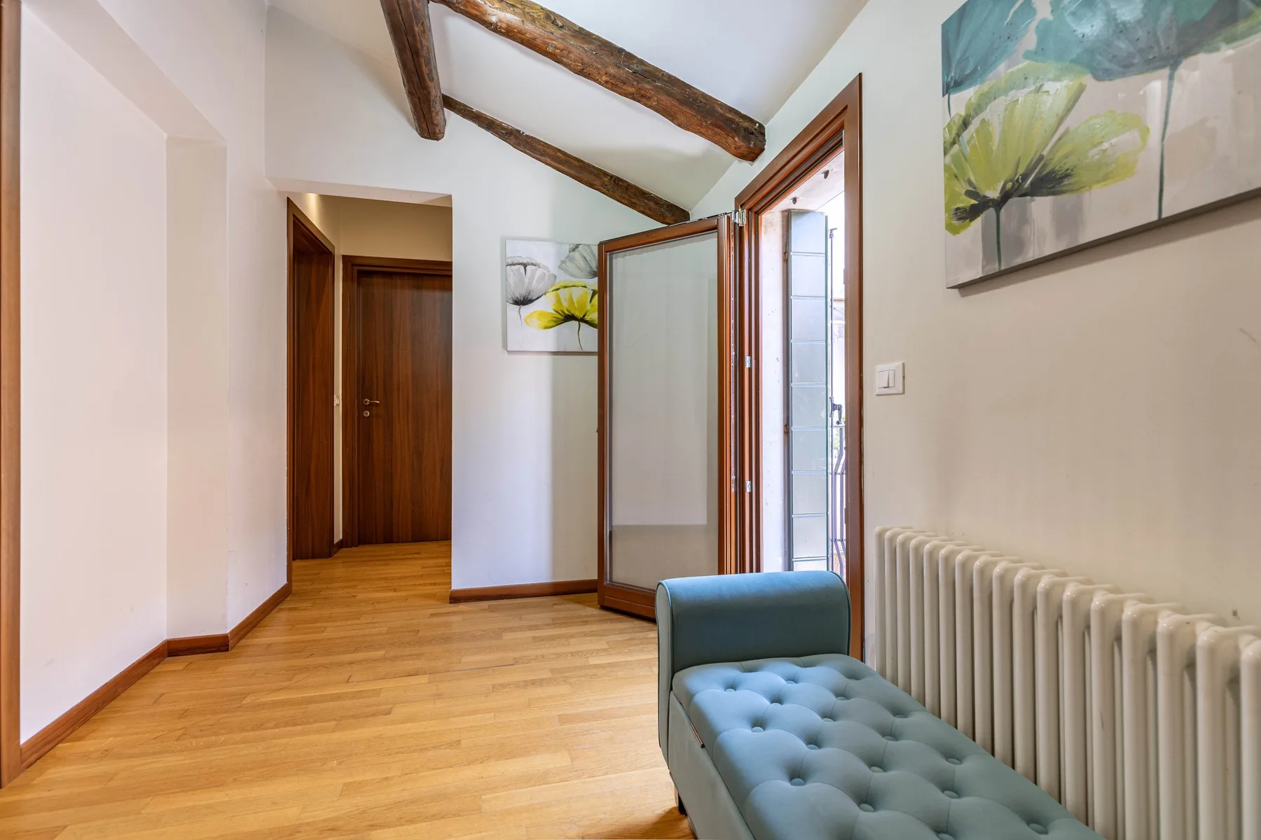 Una habitación luminosa con vigas expuestas, un banco azul y un radiador.