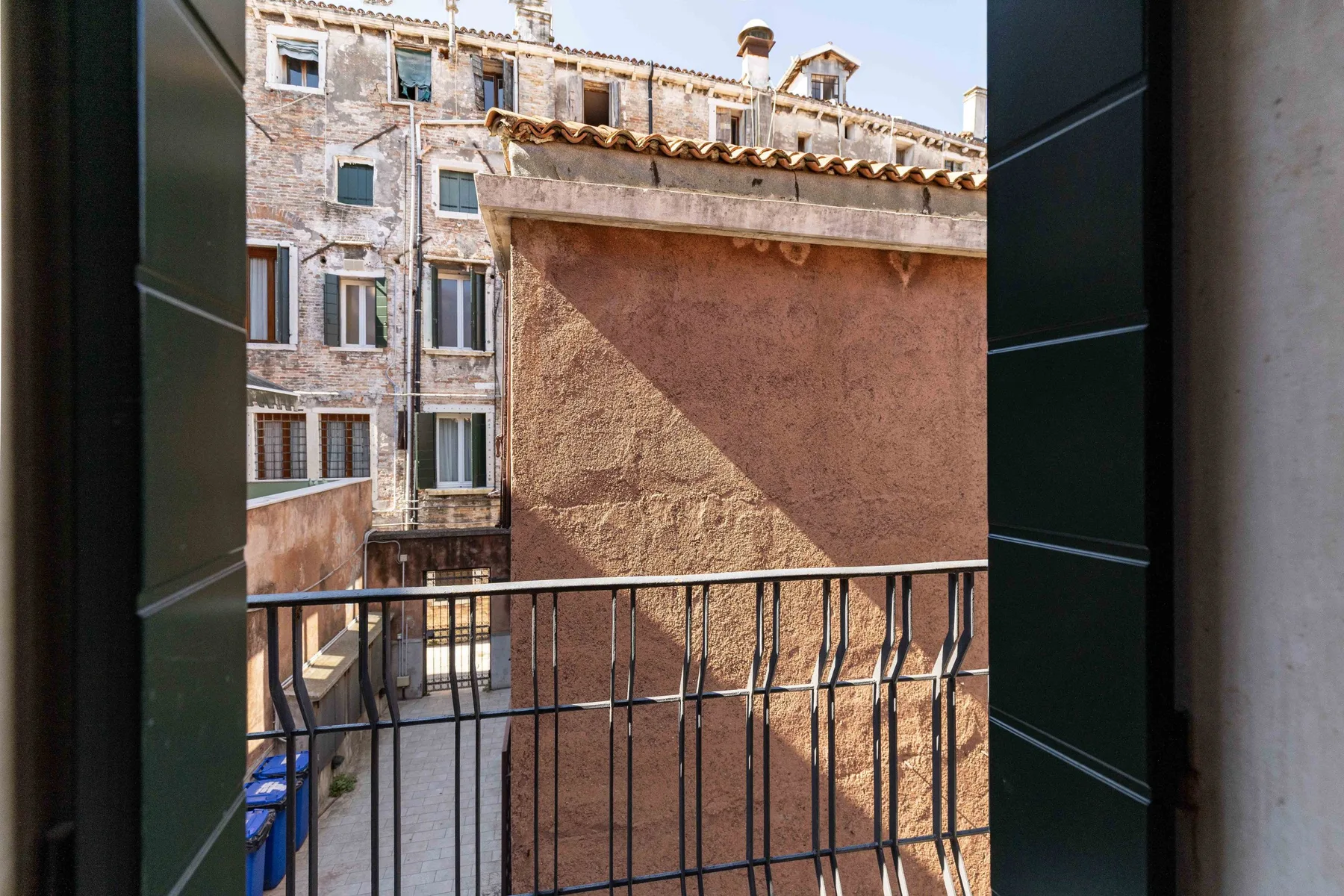 Vista desde un balcón hacia un patio estrecho y un antiguo edificio de piedra.