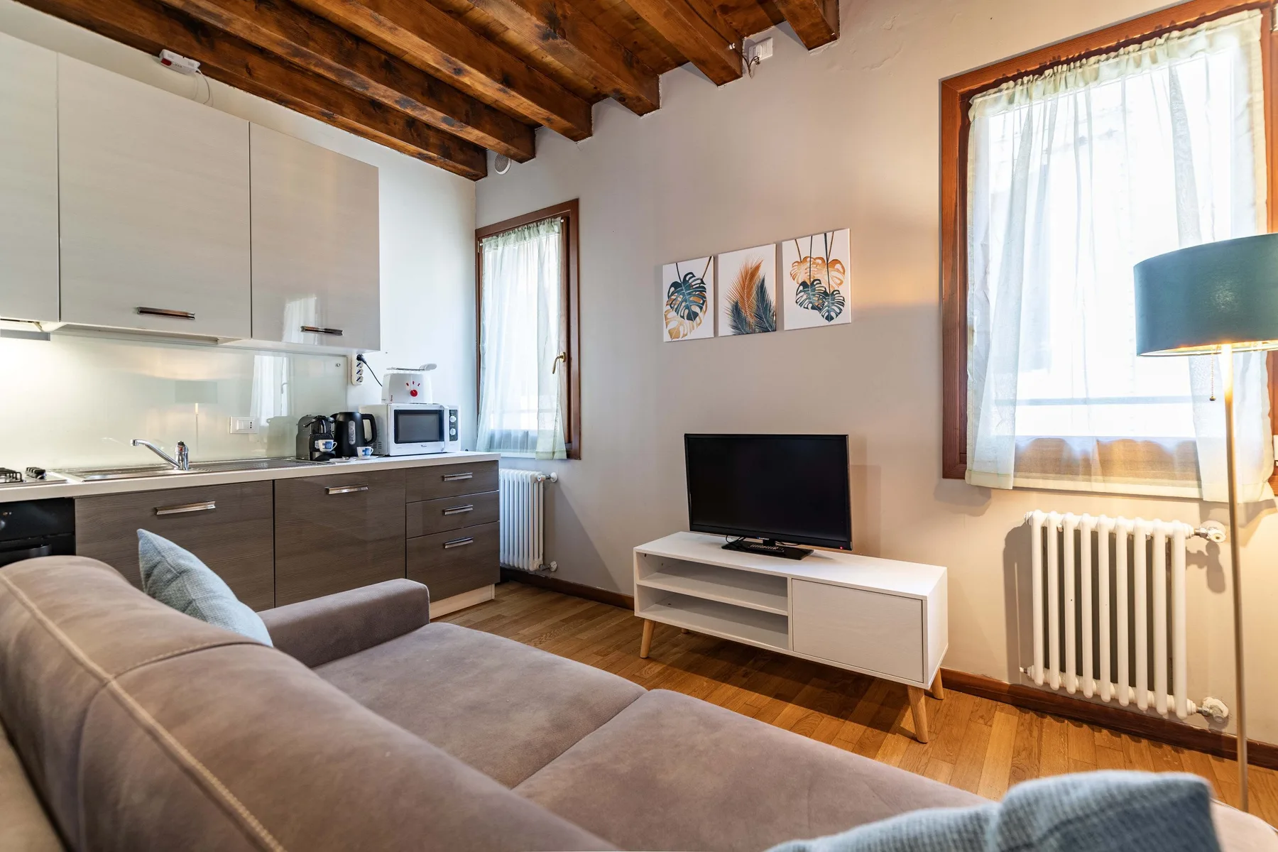 Una sala compacta con sofá seccional, televisor y cocina pequeña.