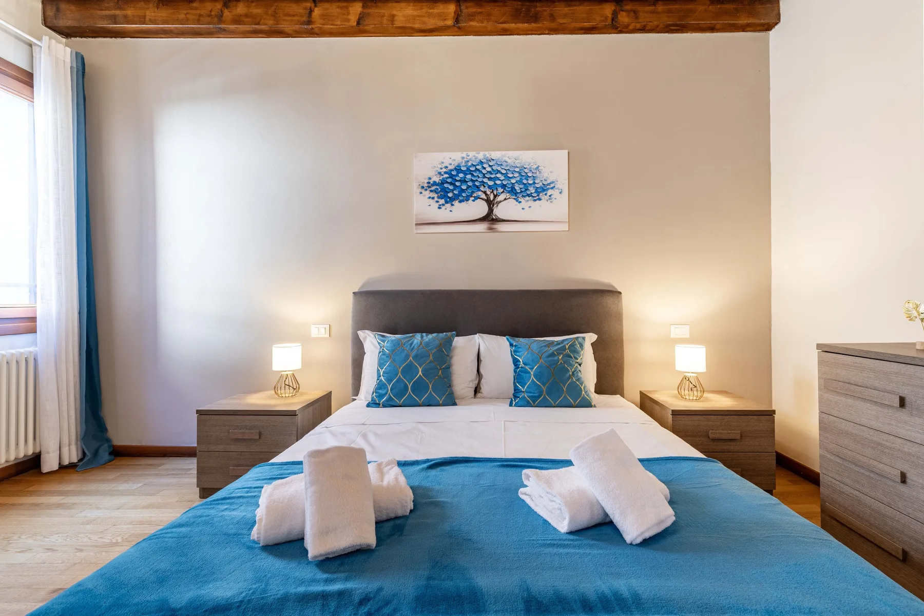 Un dormitorio con una cama vestida con ropa de cama azul y mesitas a los lados.