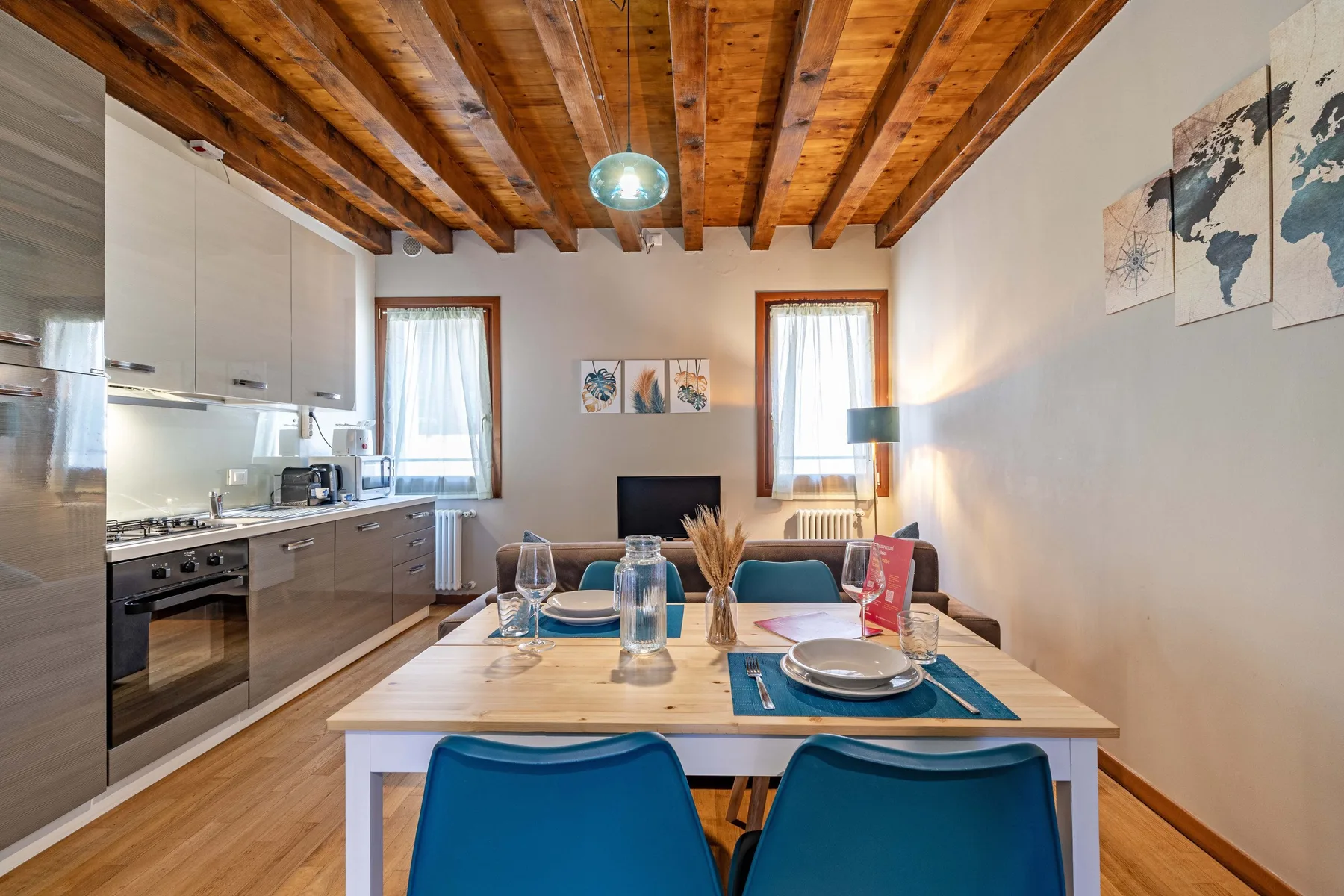 Comedor con una mesa de madera y asientos azules junto a una cocina abierta.