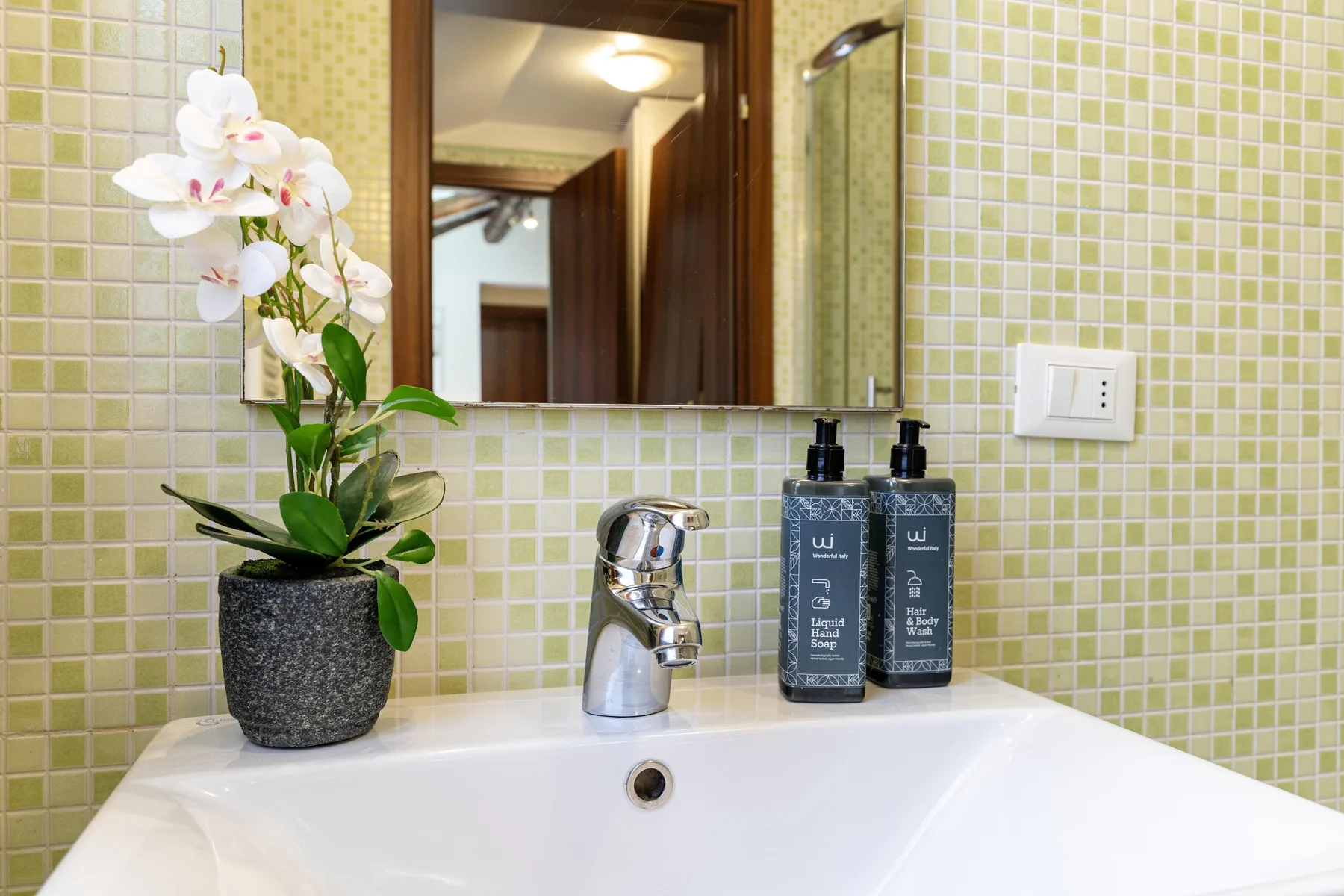 Un lavabo de baño con azulejos, grifo y orquídea en maceta.