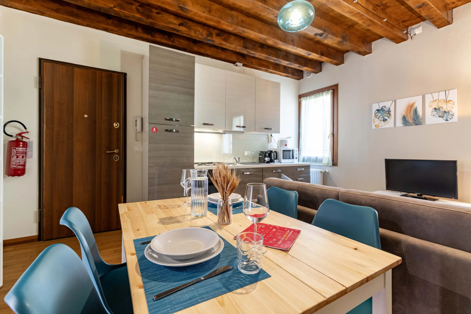 Comedor con mesa y sillas de madera, junto a una cocina compacta y una zona de estar.