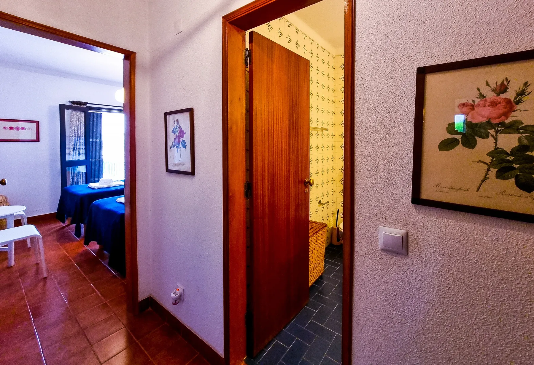 Un pasillo conecta un dormitorio y un baño con una puerta de madera abierta.