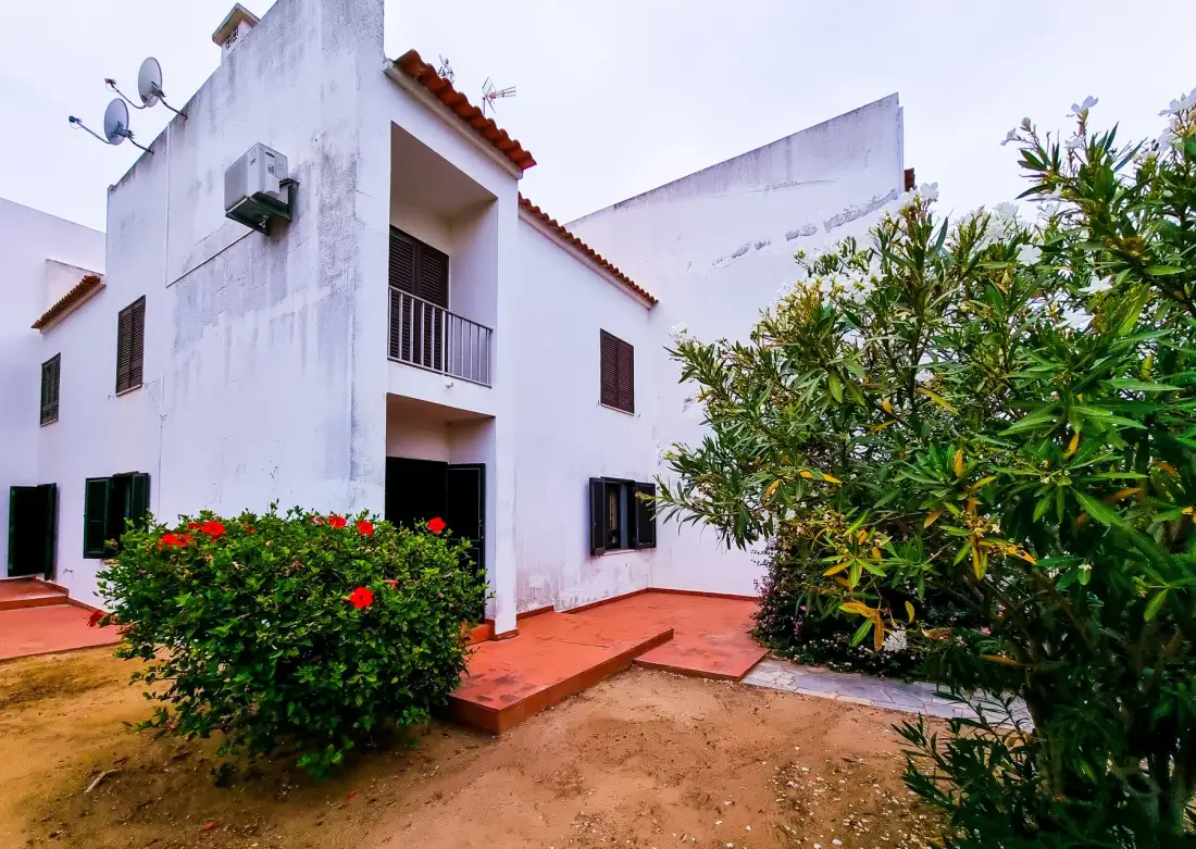 Un edificio blanco de varios niveles junto a un jardín y un patio de baldosas rojas.