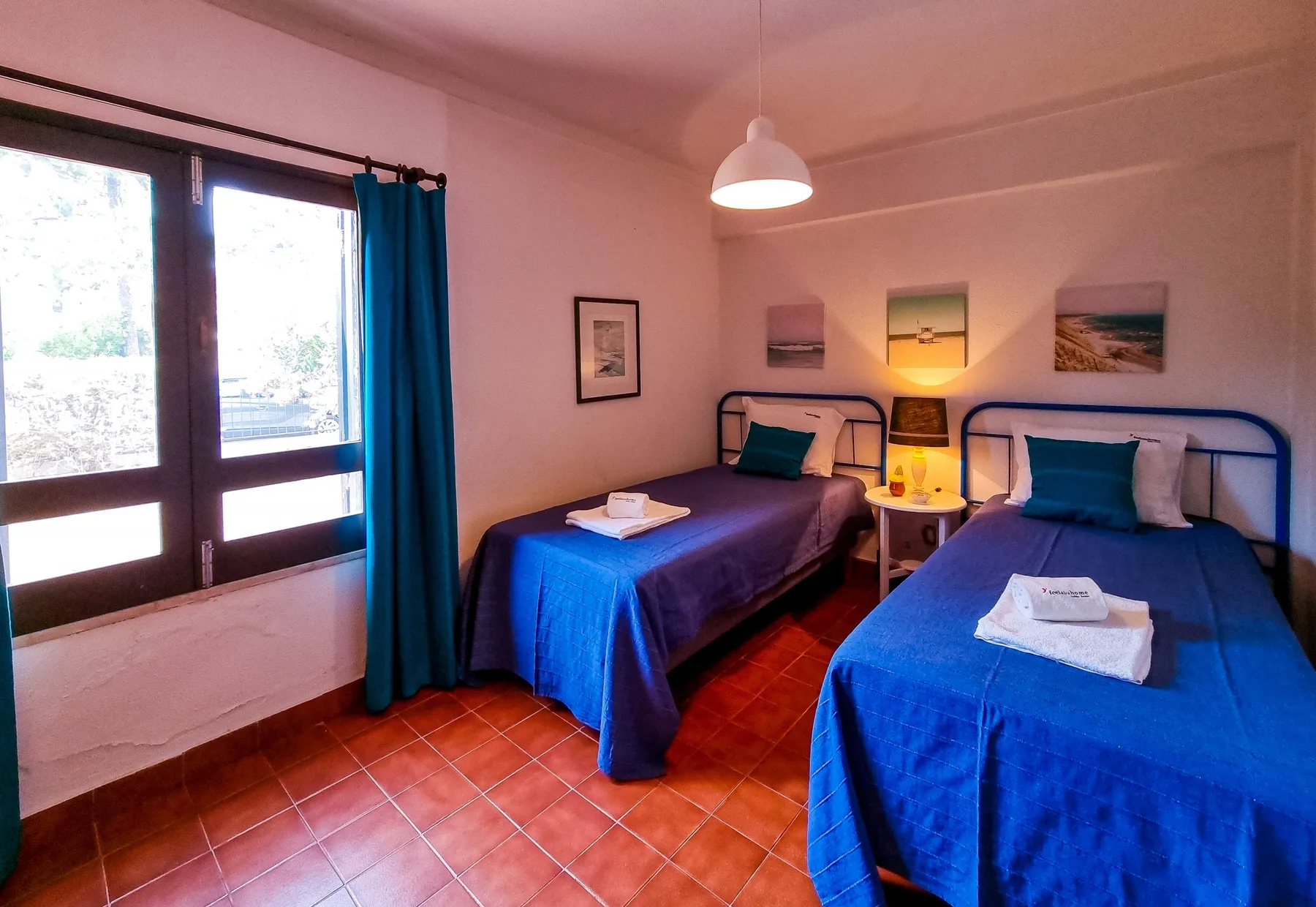 Un dormitorio con dos camas, colchas azules y una mesita de noche.