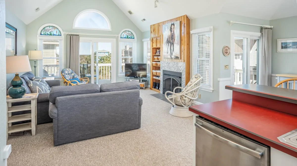 A bright living room with a seating area, fireplace, and large windows.