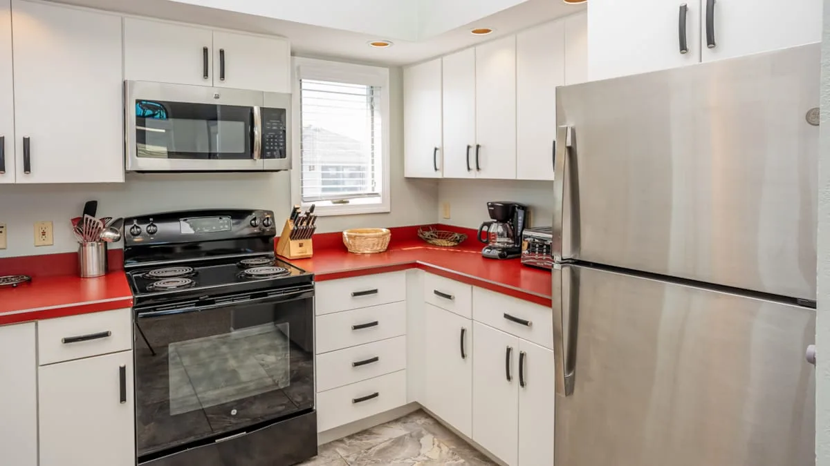 A bright kitchen with white cabinets, red countertops, and stainless steel appliances.