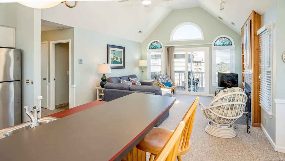 An open living area with a kitchen counter, seating, and large windows.