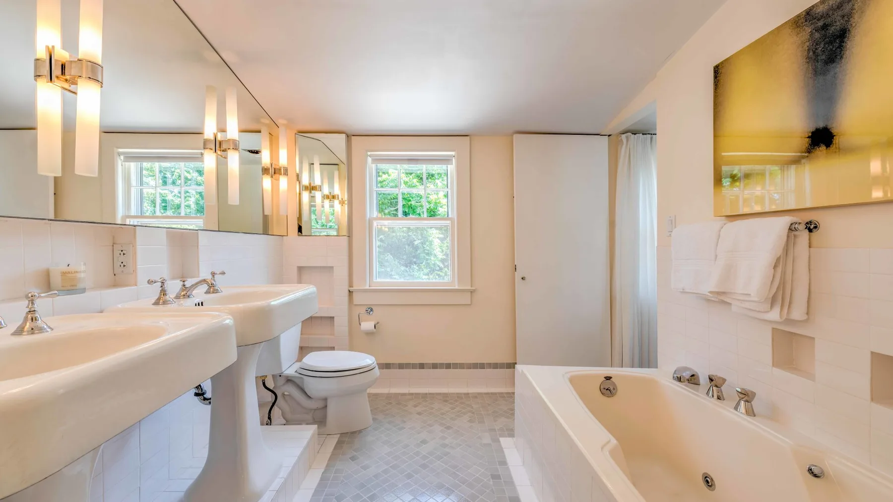 Un baño luminoso con bañera, lavabos de pedestal y una ventana.