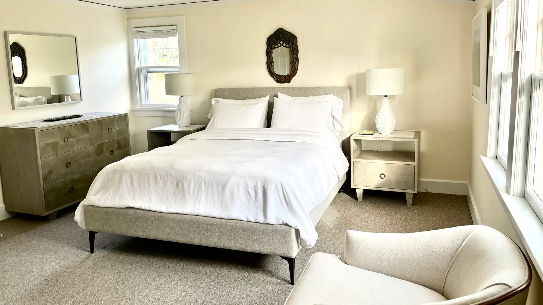 Un dormitorio con una cama, mesitas de noche y un sillón claro.