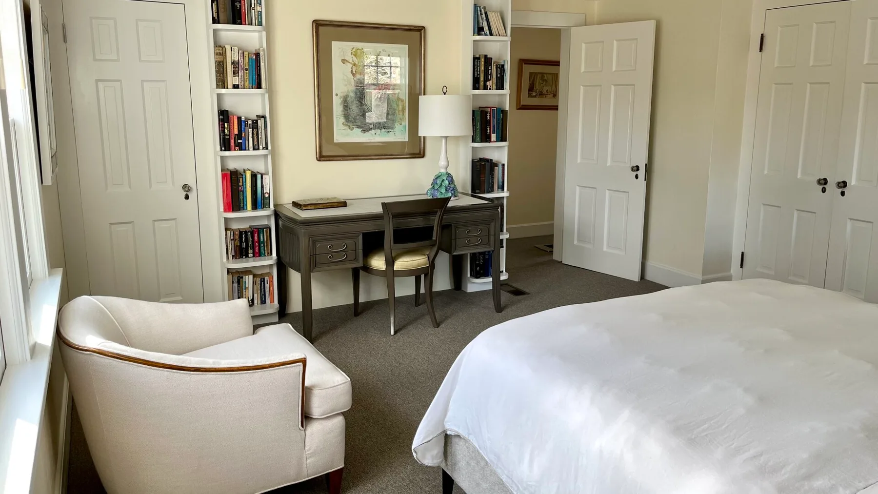 Un dormitorio con una cama blanca, un escritorio y un sillón.