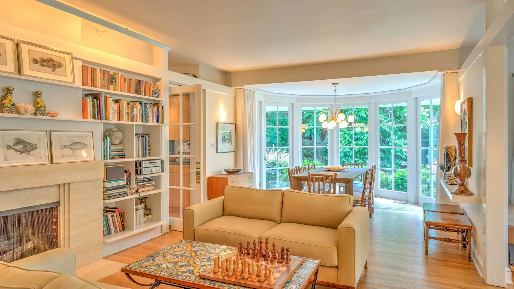 Una luminosa sala de estar con zona de descanso, estanterías y una mesa de comedor junto a grandes ventanas.