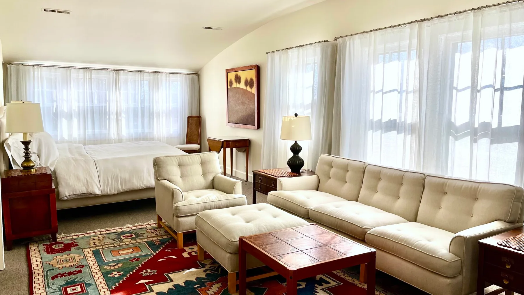 Una sala luminosa con asientos color crema, una mesa de centro de madera y grandes ventanas con cortinas.