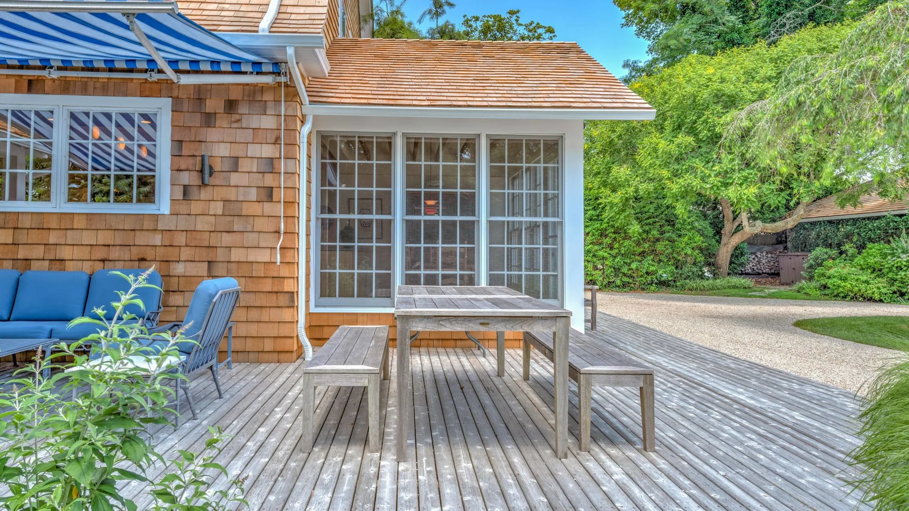 Una terraza exterior con una mesa de madera y asientos junto a una casa.