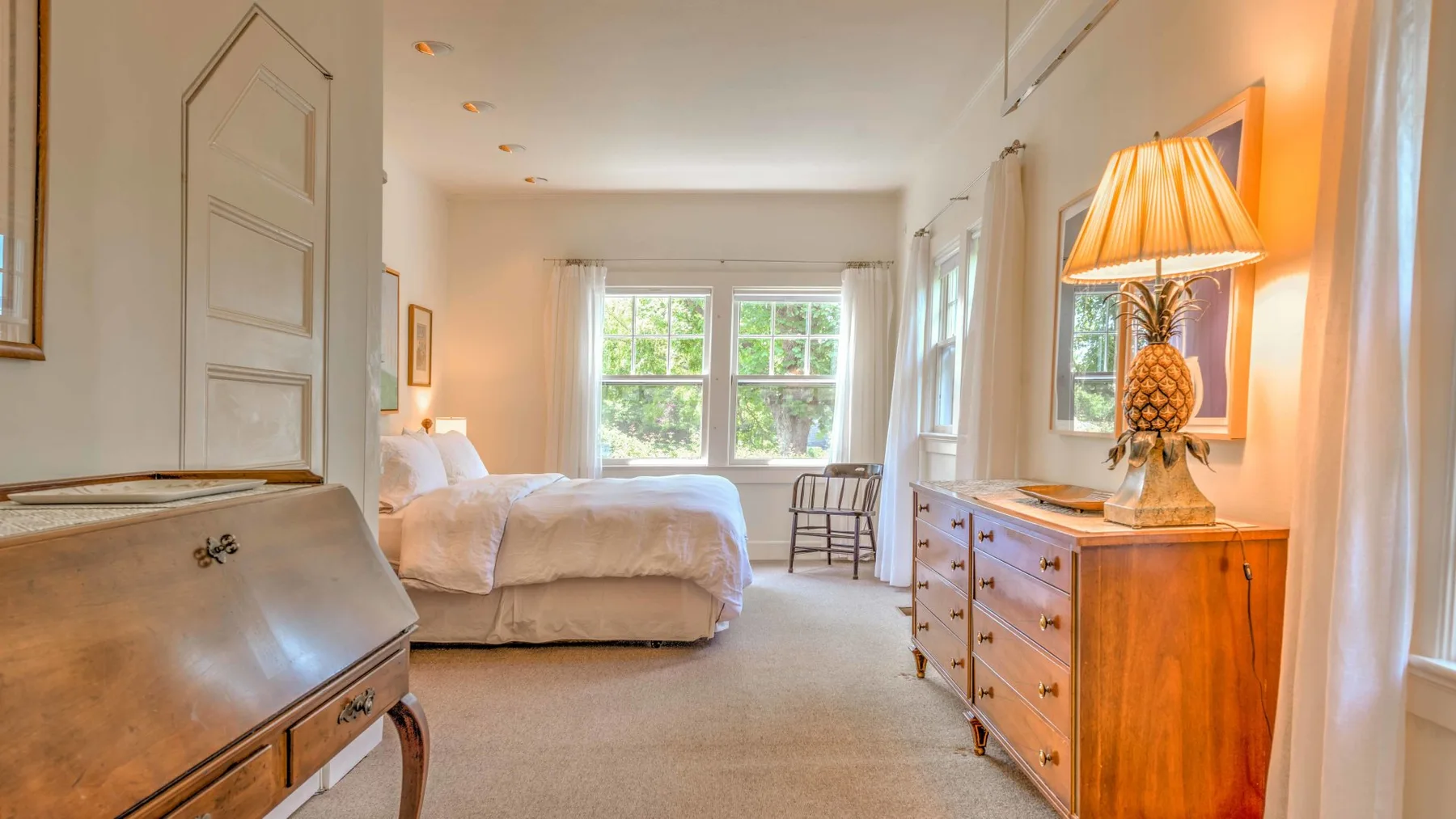 Un dormitorio luminoso con una cama, una cómoda de madera y ventanas.
