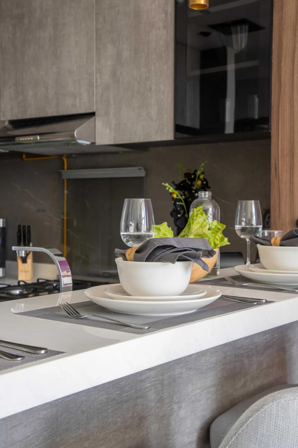 Una encimera de cocina moderna está puesta con vajilla blanca, copas y un pequeño arreglo floral.