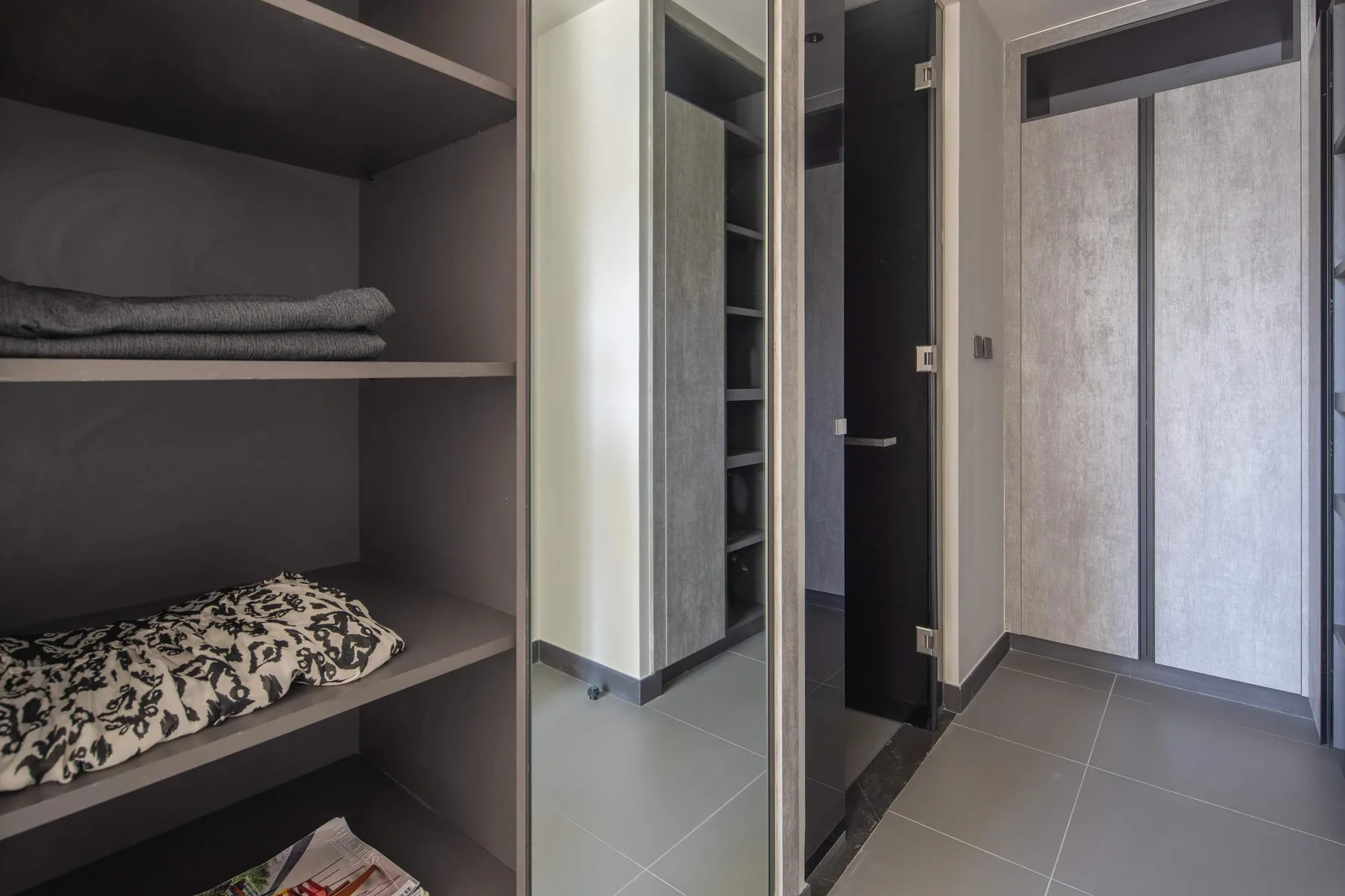 Una zona de armario con estantes abiertos, ropa de cama doblada y puertas con espejo.