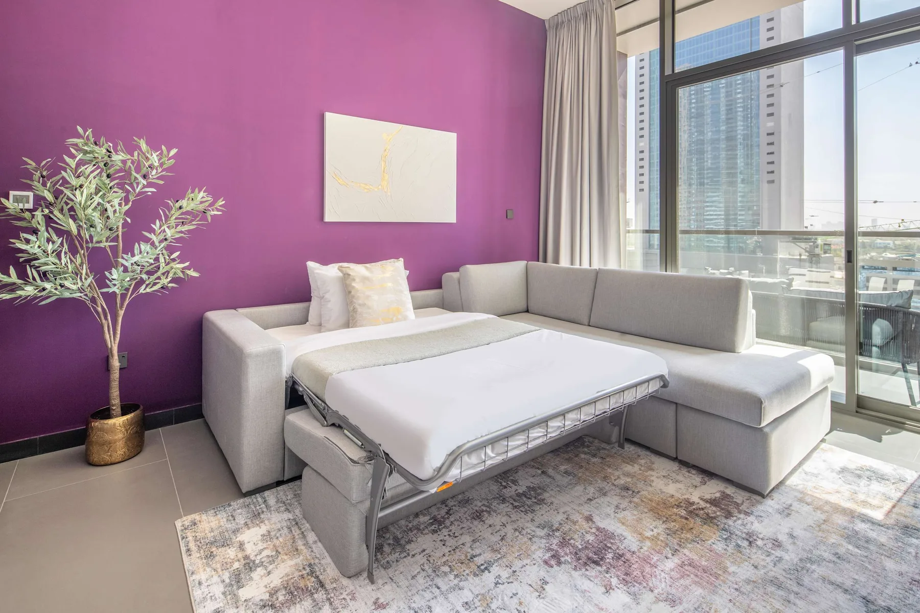 Una sala de estar con un sofá seccional gris y una cama blanca desplegada delante.