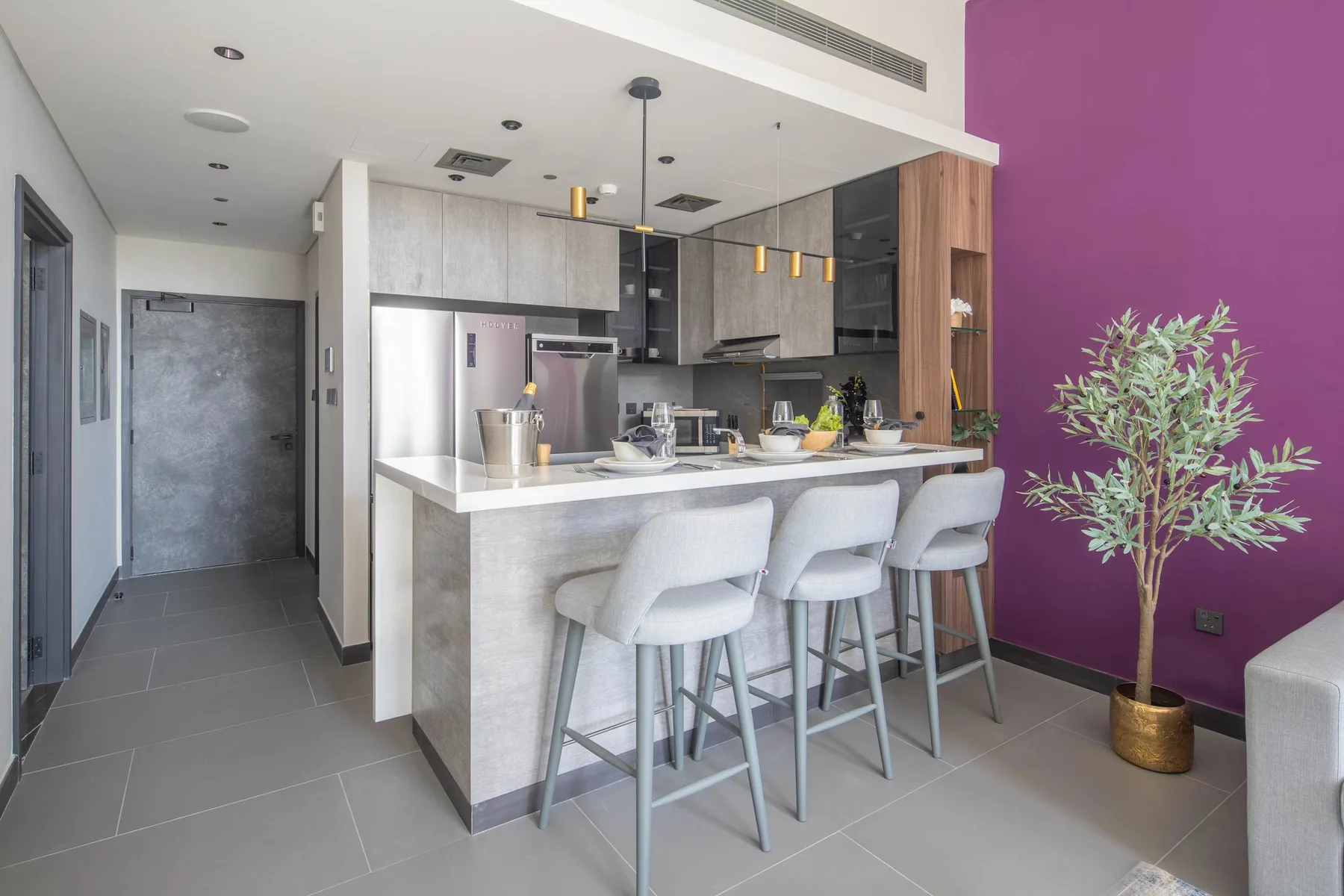Una cocina moderna con barra, asientos y una planta en maceta junto a una pared morada.