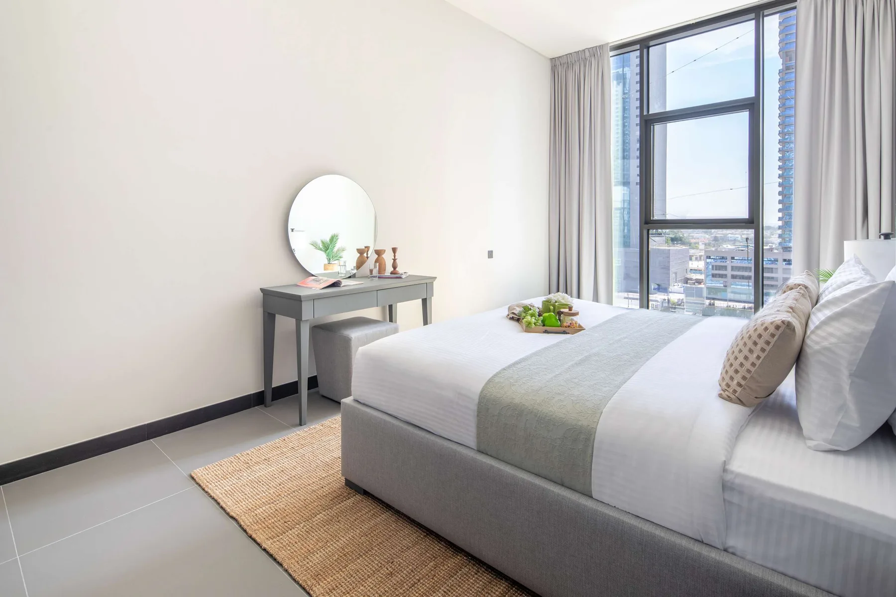 Un dormitorio luminoso con una cama bien tendida junto a una ventana grande.