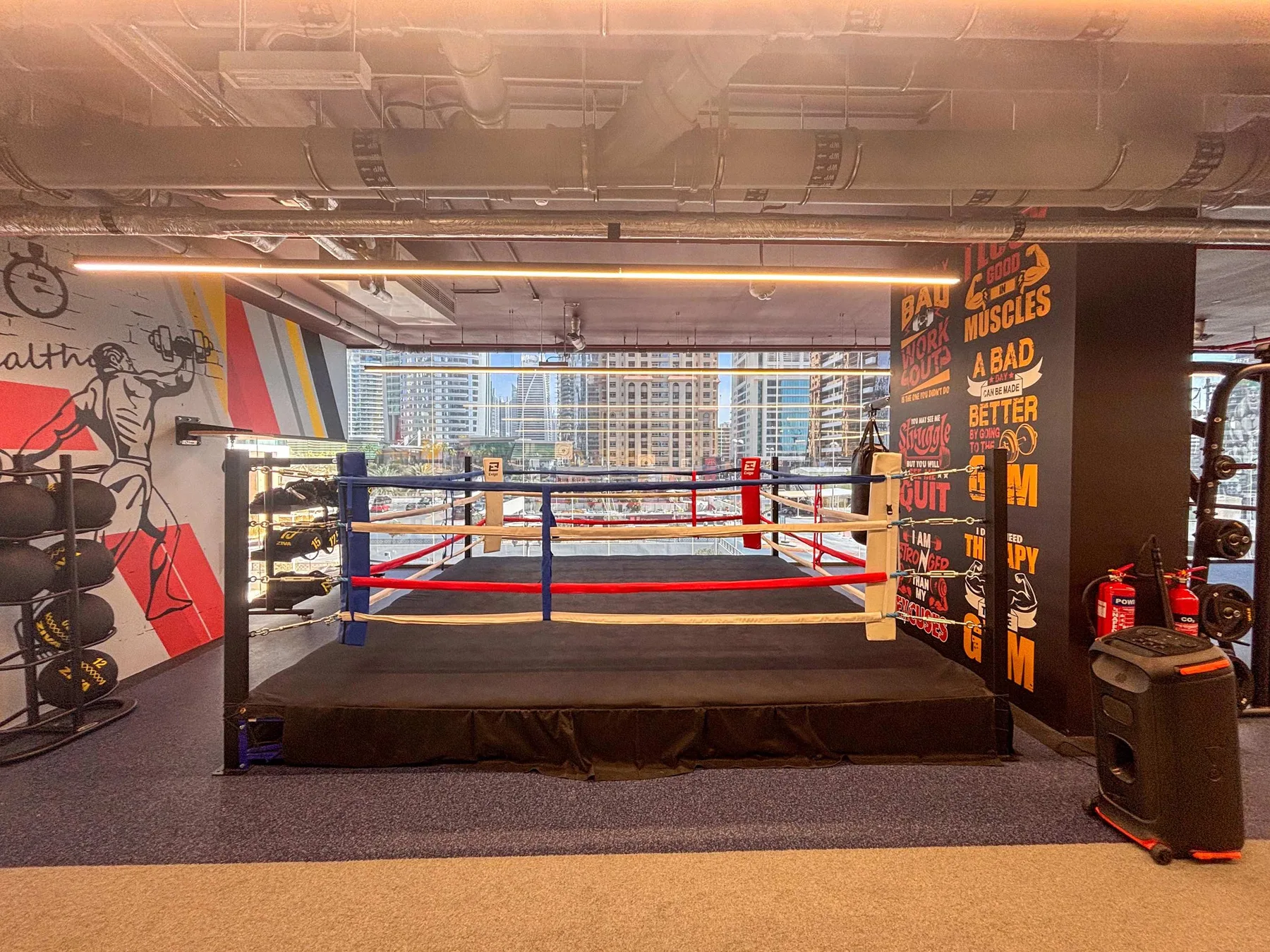 Un ring de boxeo está en un gimnasio, rodeado de murales coloridos y equipo de entrenamiento.