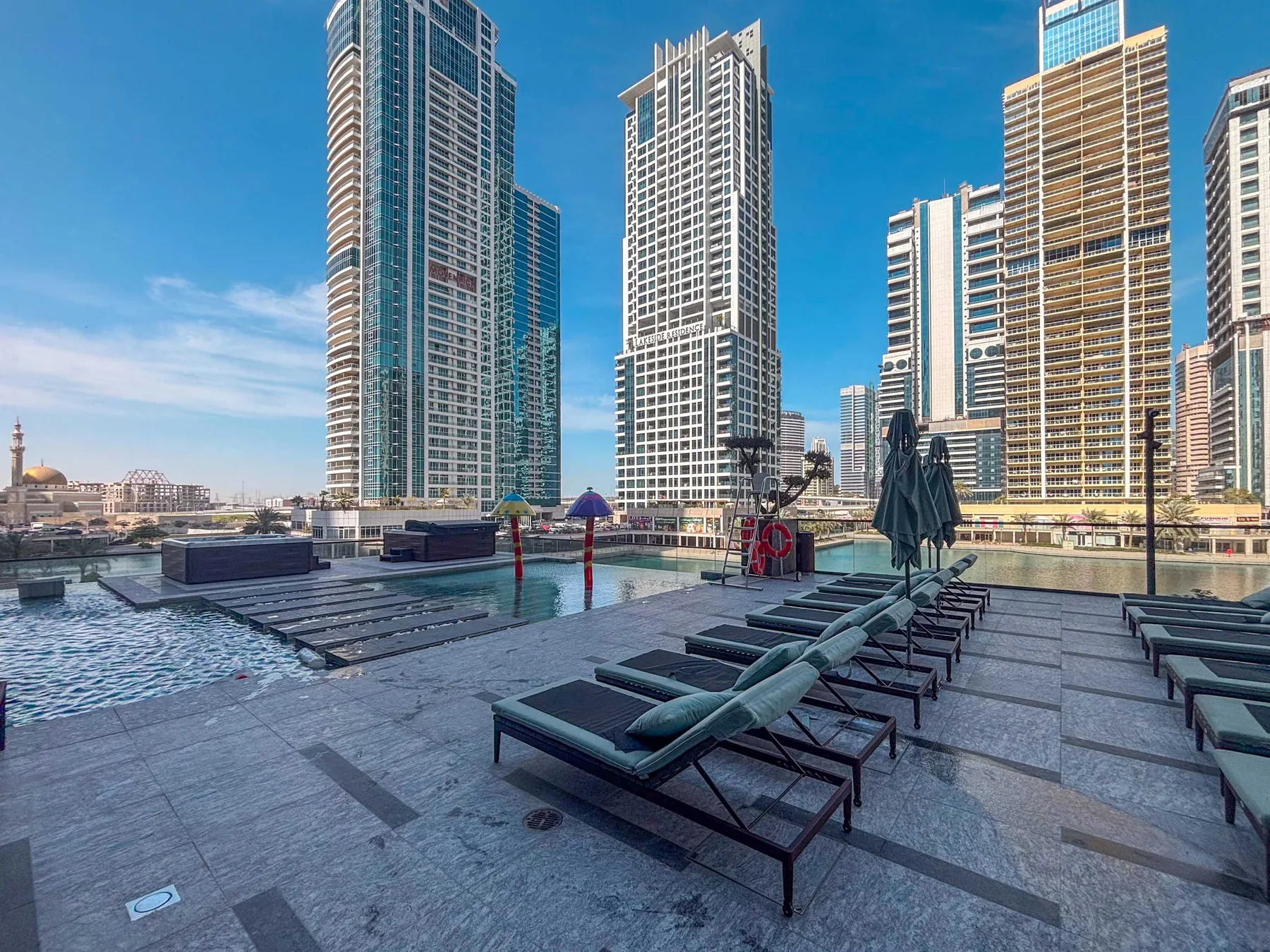 Una terraza con piscina y asientos reclinables, con edificios altos al fondo.