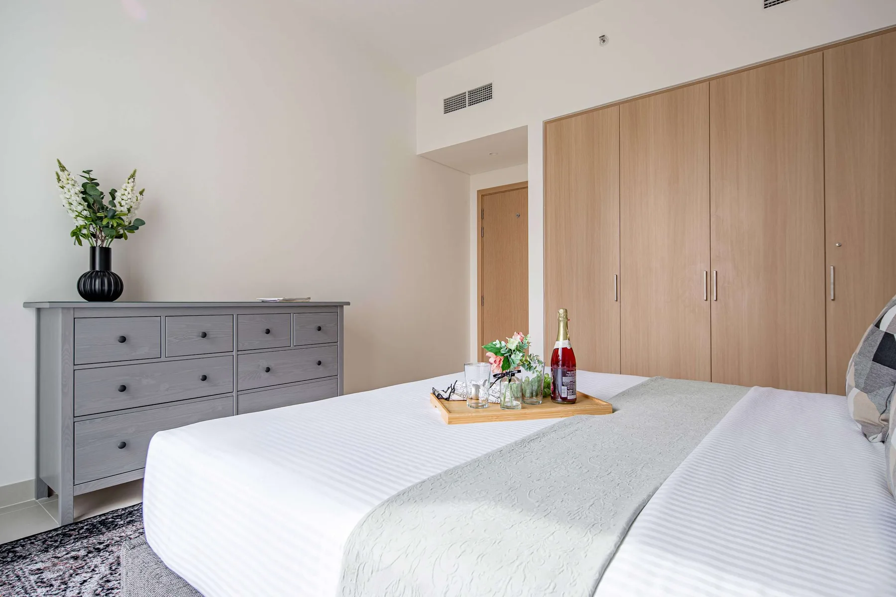 A bedroom with a neatly made bed, a dresser, and built-in wardrobes.