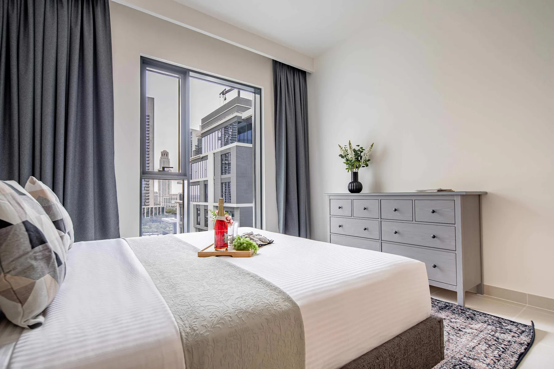 A bright bedroom with a neatly made bed and a dresser beside the window.