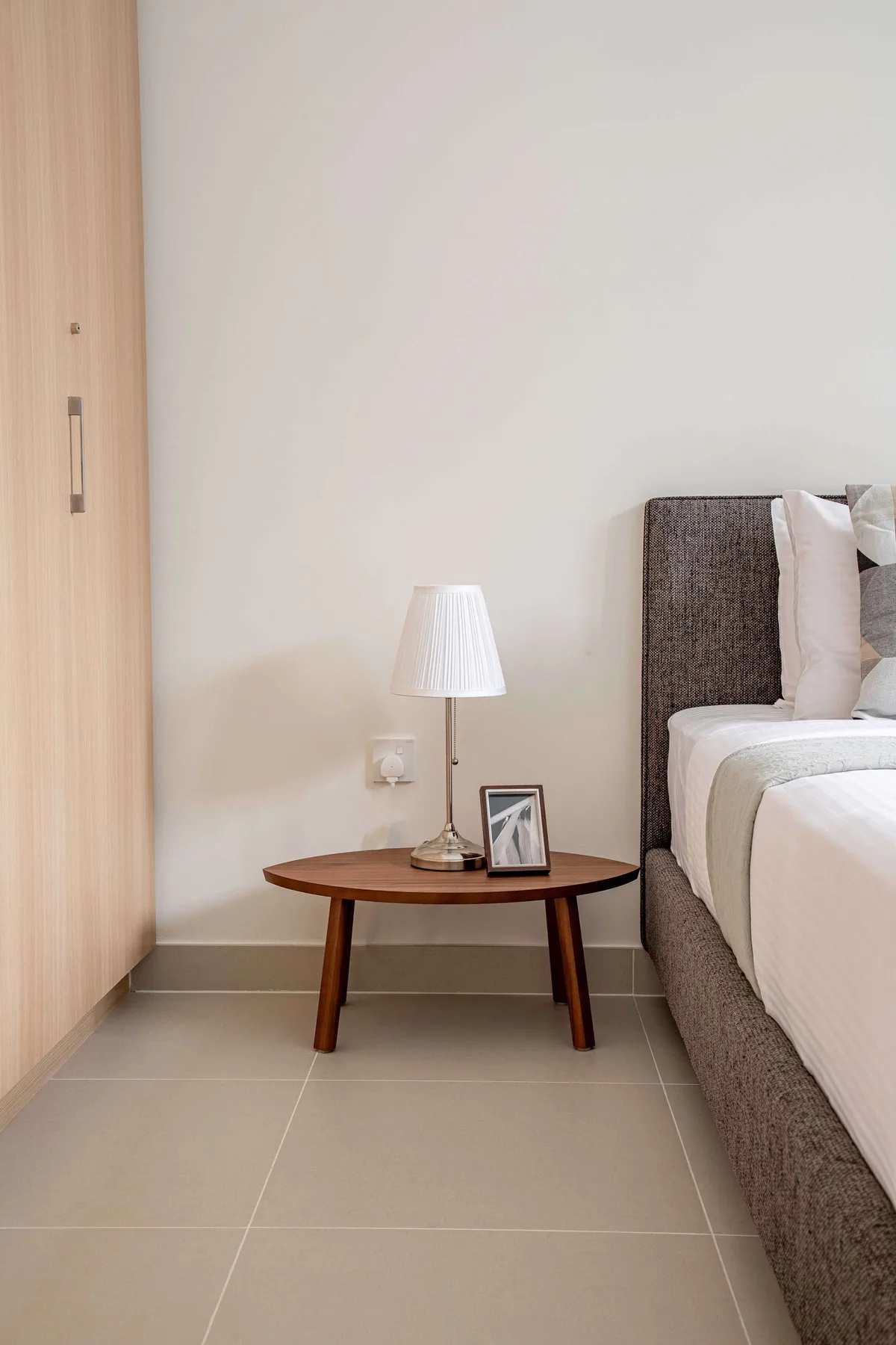 A bedroom with a bedside table, lamp, and framed photograph beside the bed.