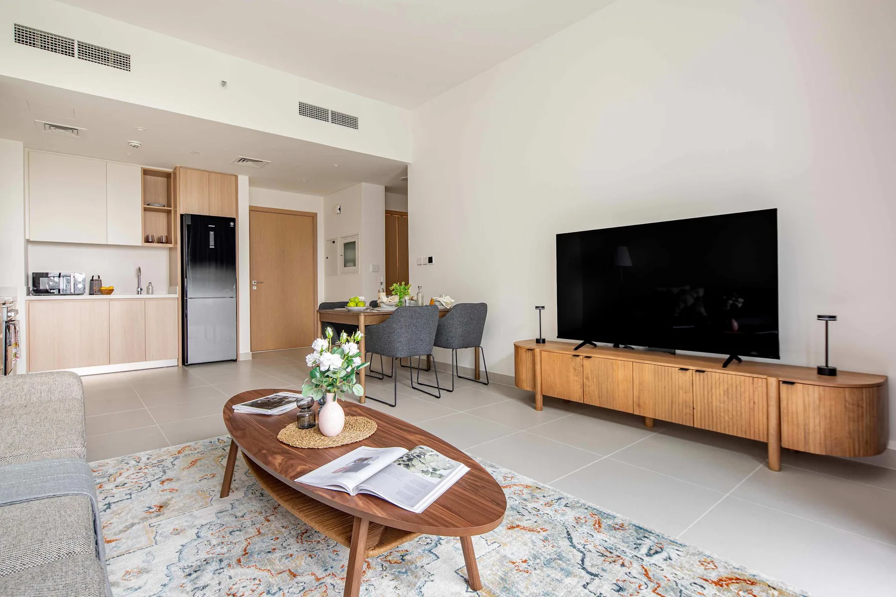 A bright living room with a television, seating, and an open kitchen area.