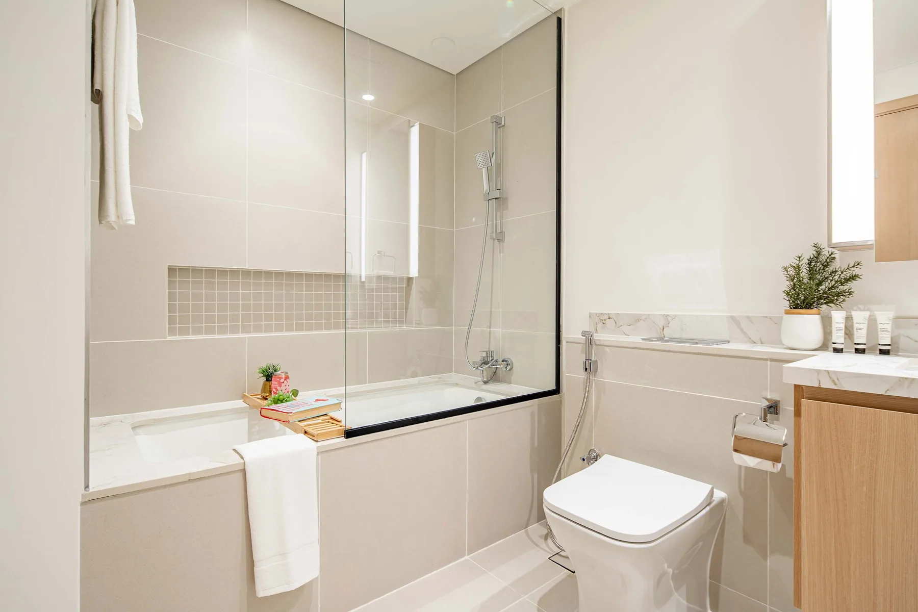 A bright tiled bathroom with a bathtub, glass shower screen, and toilet.