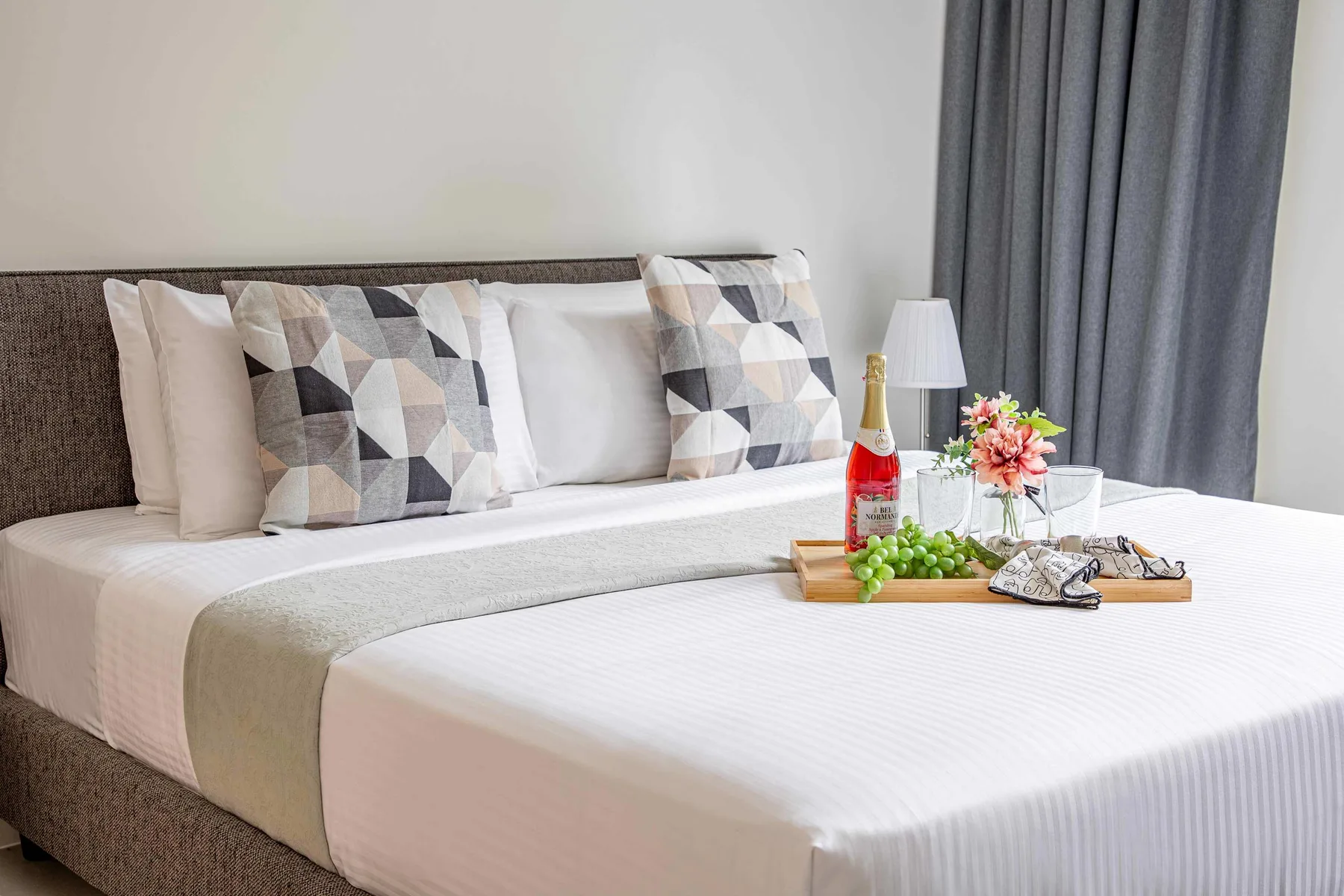 A neatly made bed with patterned pillows and a tray of refreshments.