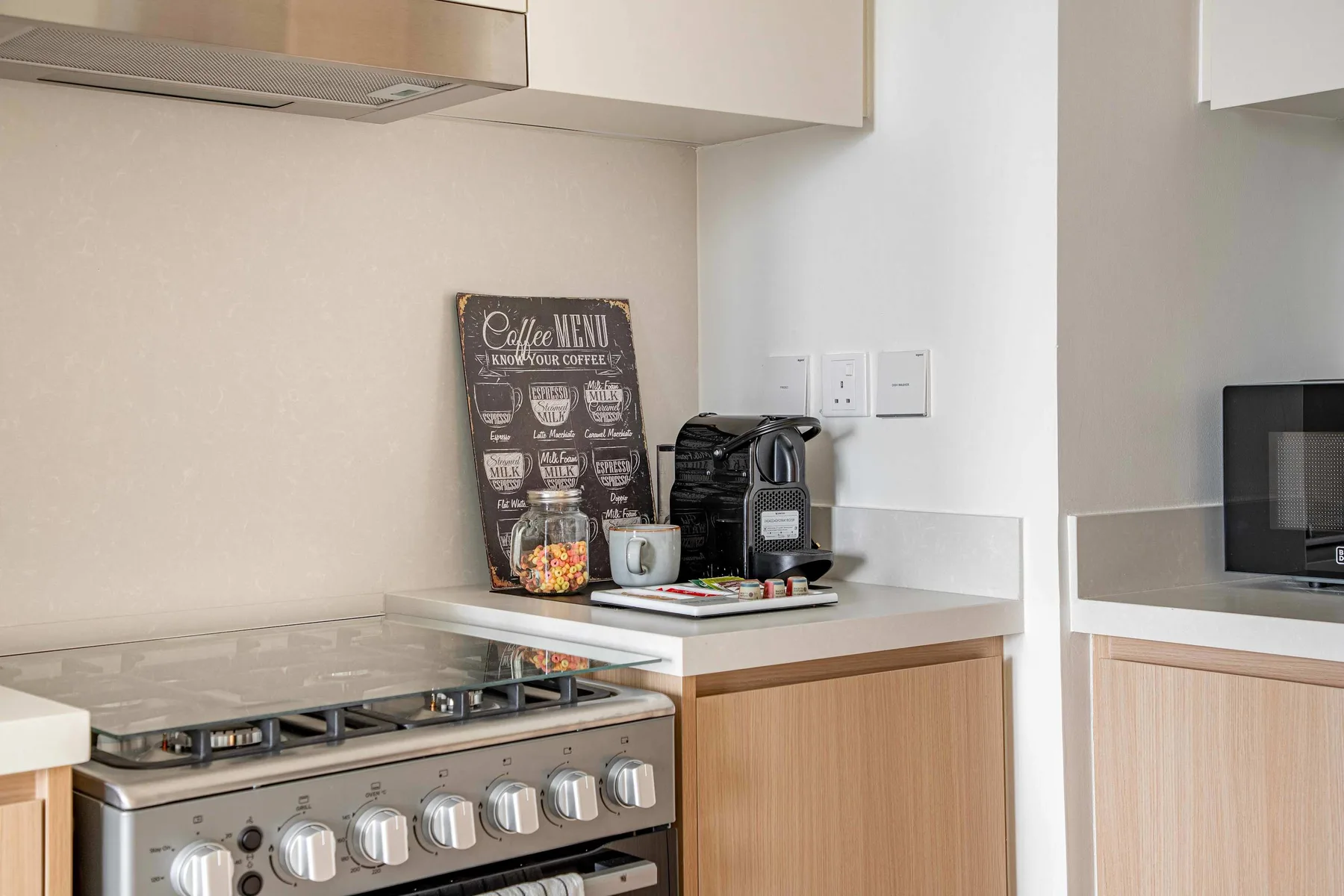 A kitchen counter with a coffee machine sits beside a stovetop and oven.