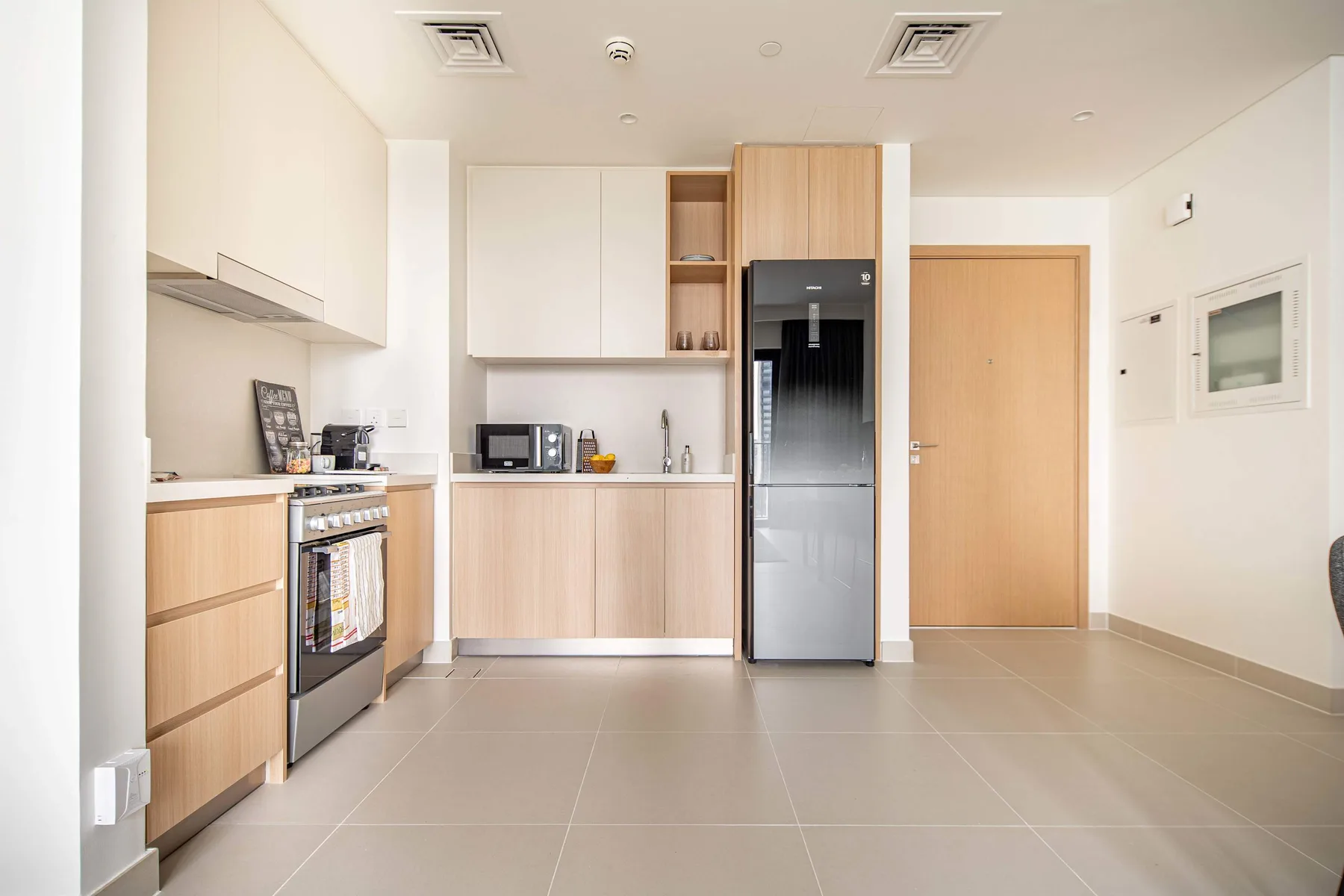 A modern kitchen with light cabinetry, a refrigerator, and a tiled floor.