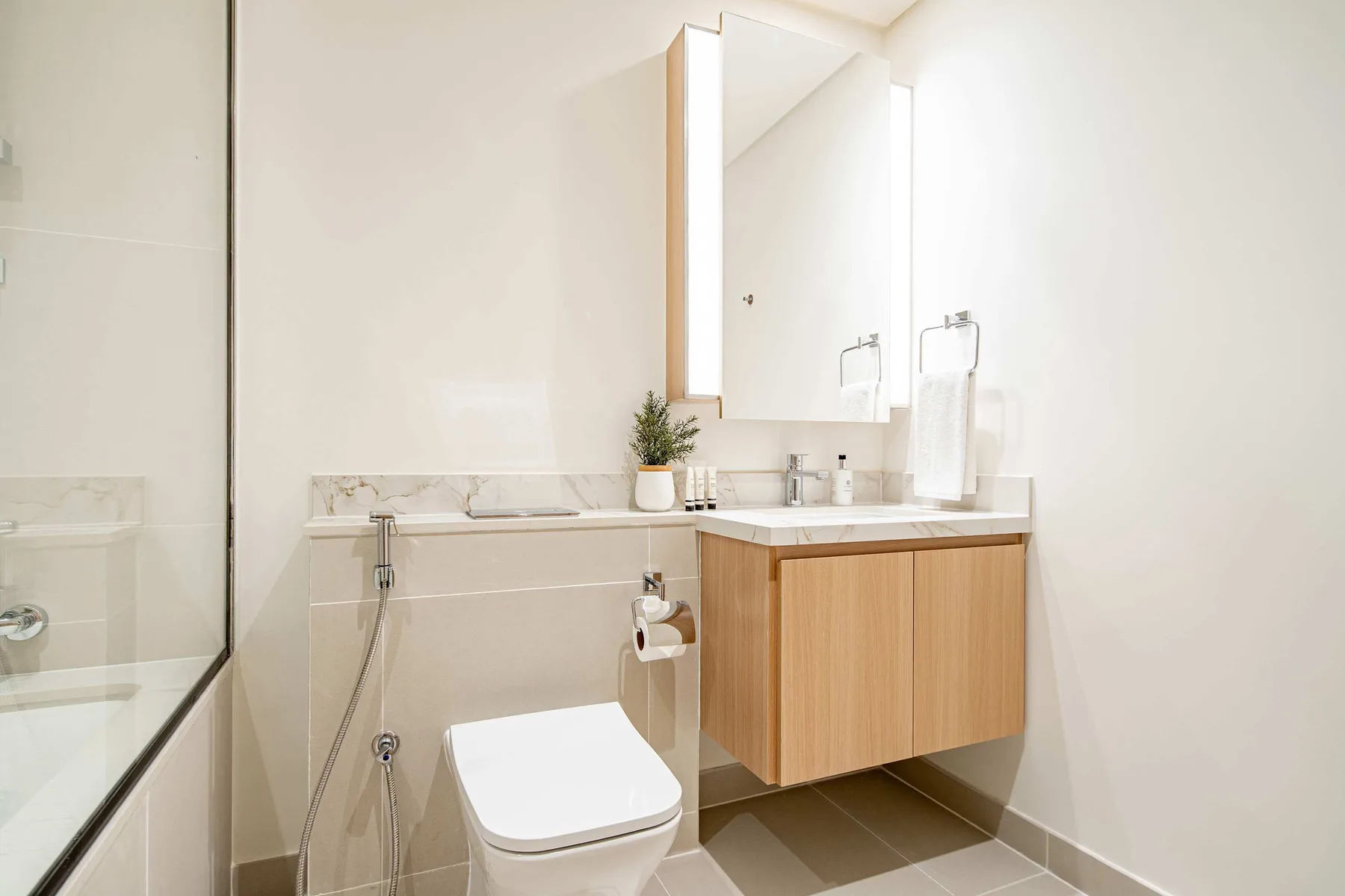 A bright bathroom with a toilet and a wood-fronted vanity beneath a mirror.