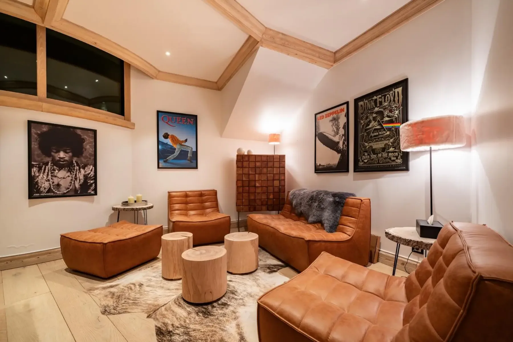 Cozy room with brown leather chairs, wooden stools, music posters on walls, cowhide rug, and warm lighting.
